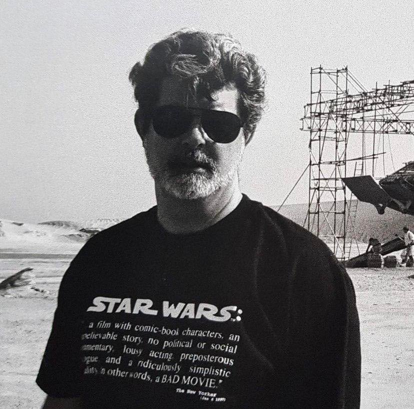 George Lucas wearing a shirt adorned with a bad review of #StarWars on the set of ‘The Phantom Menace'