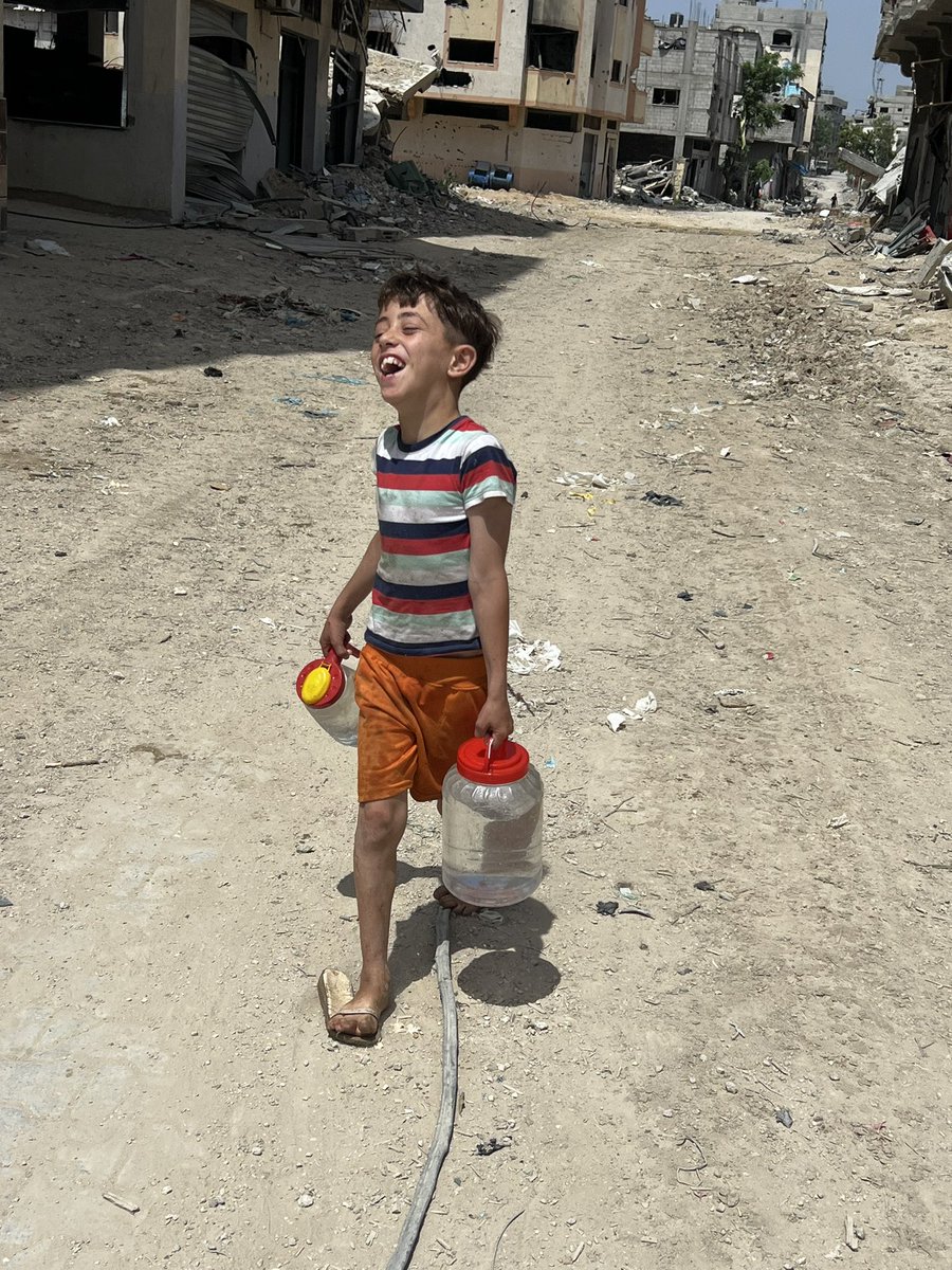 La triste felicidad de un niño palestino sin zapatos que sonrie por las devastadas calles de Gaza porque pudo llenar dos frascos pequeños con agua limpia por primera vez en 6 meses. En Gaza, el agua y la comida se convirtió en un lujo, mientras los colonos sionistas que los