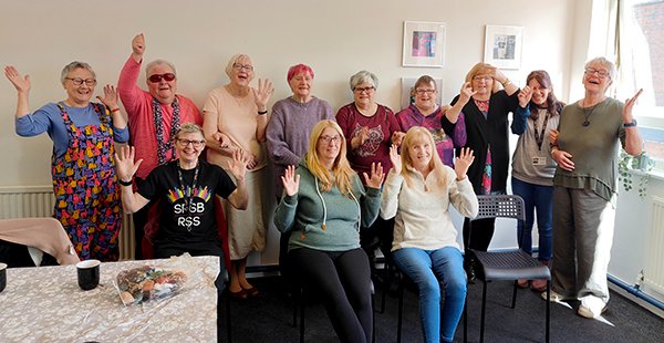 Hurray! Our first Craft Group group at RSS since we finished the refurb! So good to welcome everyone back. Photo shows members of the group and a staff member, standing/sitting in the new craft room at RSS, they are all smiling and some waving their hands in the air