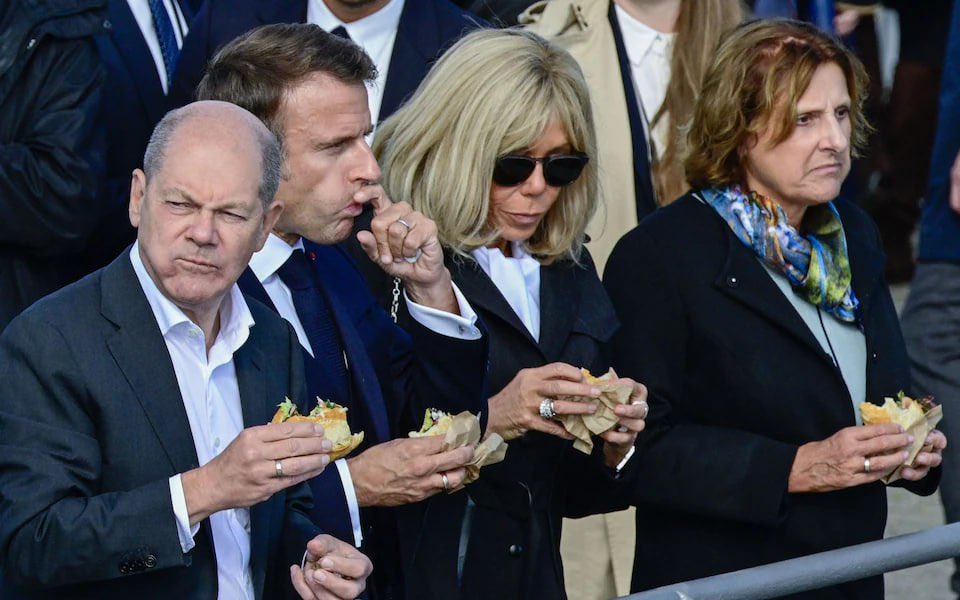 A photo of German Chancellor Olaf Scholz and French President Emmanuel Macron, along with their wives. What do you notice?