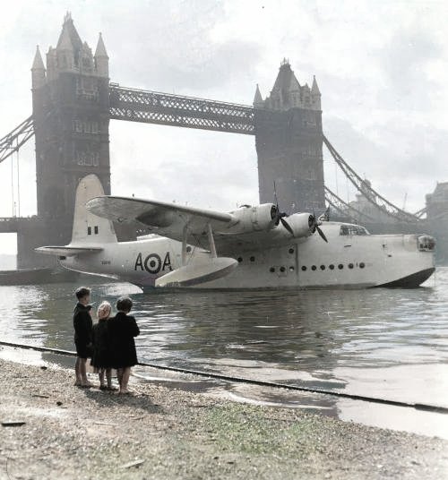 Three kids on Tower Beach watching a Short Sunderland flying boat on the River Thames at Tower Bridge during the Battle of Britain week celebrations in 1951.