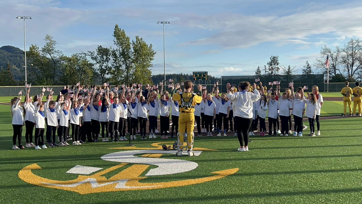 Wade King choir students stand on the field at Sehome High school, led by staff member and Sehome baseball player while singing.