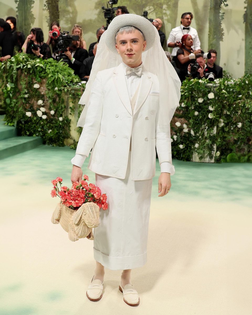 … cole … cole escola wears a thom browne spring 2021 archival runway double breasted sack sport coat in white diamond pique with white grosgrain tipping and medium crest embroidery, ankle length belt loop skirt in white linen with small crest embroidery, cable knit vest in…