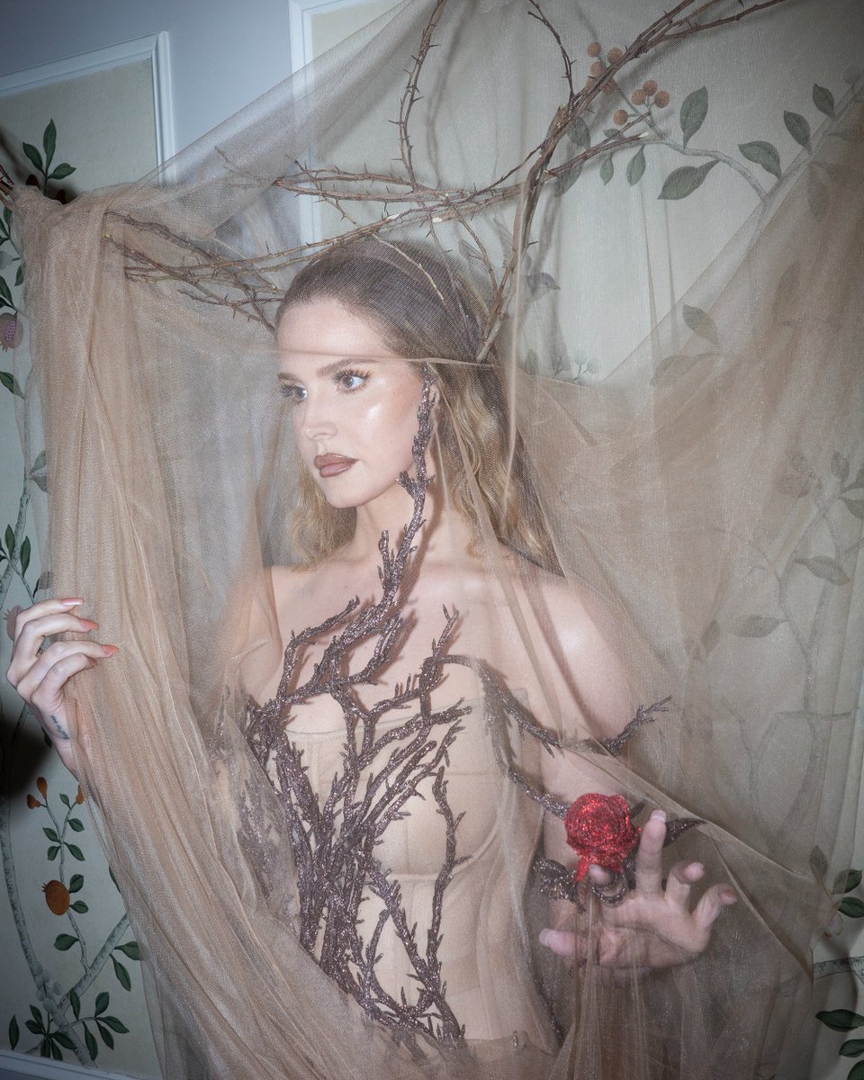 Ahead of the 2024 #MetGala, #LanaDelRey wears a custom-made Alexander McQueen corseted dress with hand-embroidered bronze hammered bullion hawthorn branches, a headpiece made by hand using natural hawthorn branches and draped with a veil of tulle, completed with Hoof boots.