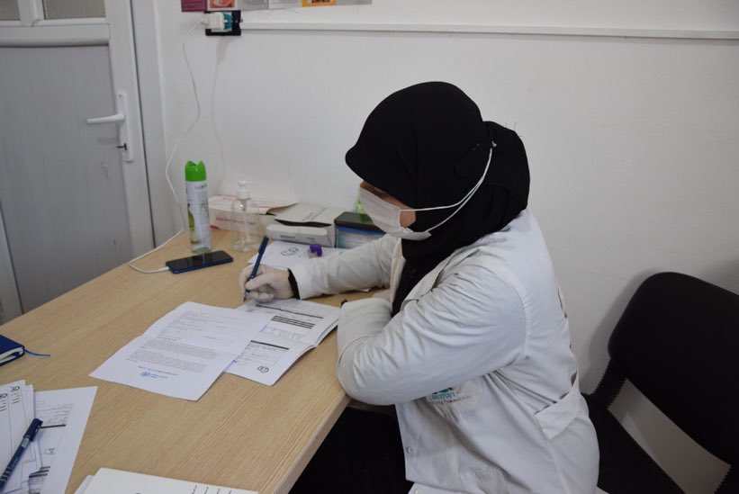 Aliyah, a paediatric nurse in northern Aleppo, has been displaced six times due to the conflict. She lives in a temporary shelter with harsh conditions and safety risks. She wears bags over her uniform while traveling to keep herself clean and protected.