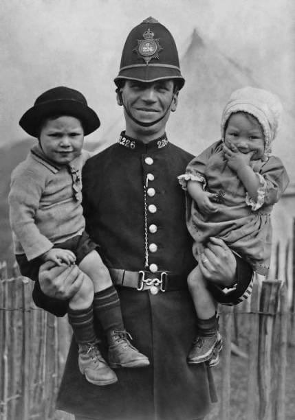A photograph of a policeman with two lost children at a bank holiday event on Hampstead Heath, London, taken circa 1925.