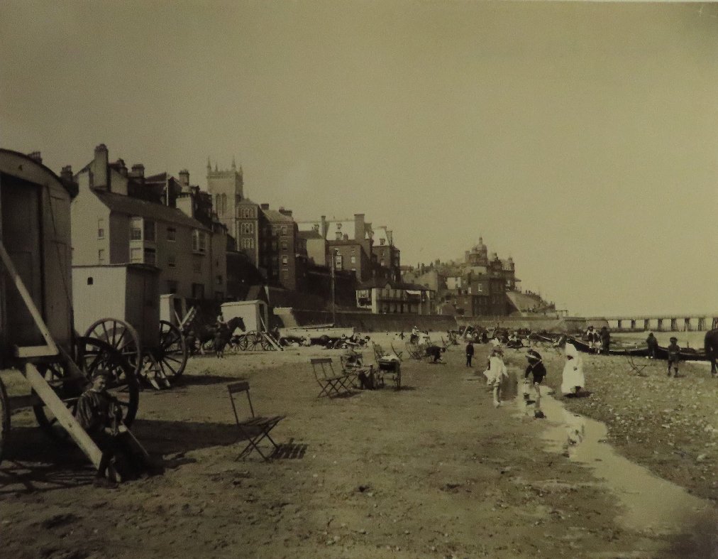 Photograph taken from the Red Lion Steps, East Cliff, #Cromer, looking down along the East Beach to the Jetty and along the lower promenade to the Bath Hotel, on the beach some children are paddling. 1894-1897.