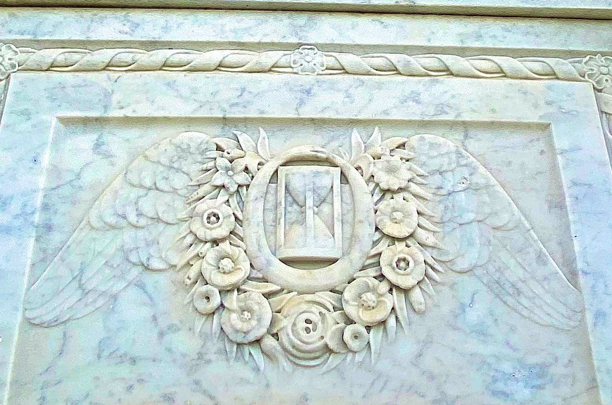 The Dupaquier family tomb’s marble closure tablet features an ornate relief carving depicting a winged hourglass encircled with a floral wreath.  The hourglass is surrounded by a snake eating its tail (ouroboros), a symbol of immortality. St. Louis Cemetery #3, New Orleans, La.