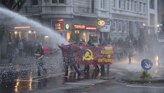 Communists marching in the streets on the first of May. The banner shows the slogan 'Against oppression and exploitation' and the terrifying communist hatesymbol, symbol of misery, robbery, lies,  concentrationcamps, hunger, slavery, massmurder and oppression and exploitation.