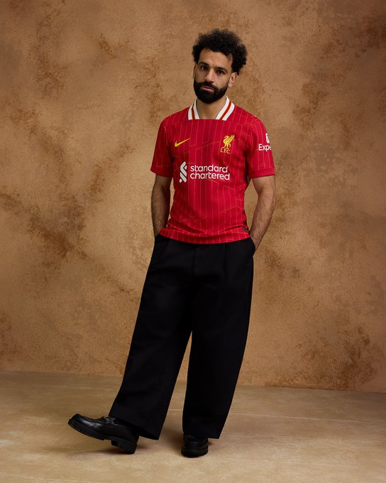 Mo Salah poses in our new 2024/25 home kit. 

The red jersey features a chrome yellow pattern design which sees a modernised take on the legendary '84 home shirt, a season which saw the Reds become European Champions for the 4th time in Rome and the first English Club to win a Treble of major honours.