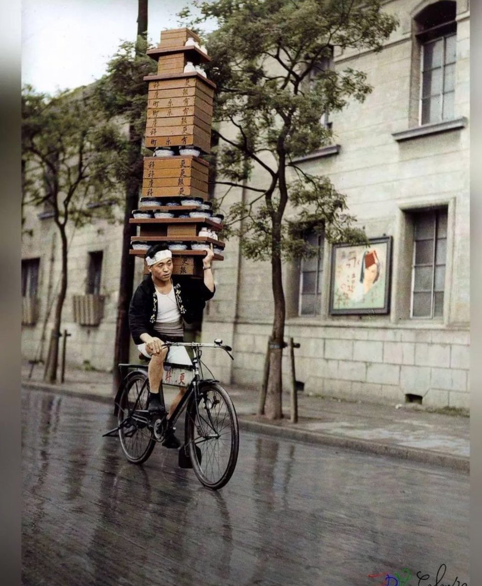 A Japanese man photographed riding a bicycle while carrying soba noodles on his shoulder in Tokyo, Japan in 1935
