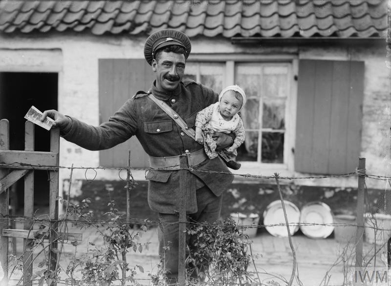 British soldier holding a baby outside a cottage in Adinkerke, 6th August 1917. Adinkirke is 20km east of Dunkirk.