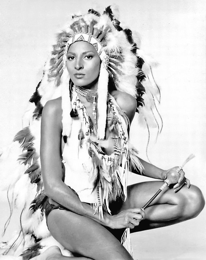 1985, Pam Grier, whose mother hailed from the Cheyenne tribe, is captured wearing a traditional Native American headdress in a photograph taken by Harry Langdon.