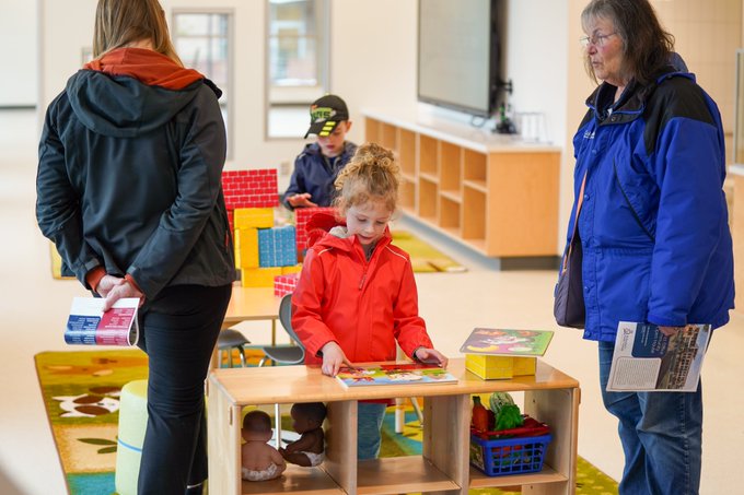 Two young children play in the early learning center with adults looking around