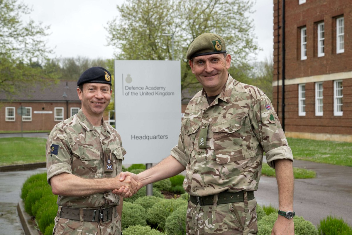 Two army officers shaking hands outside.