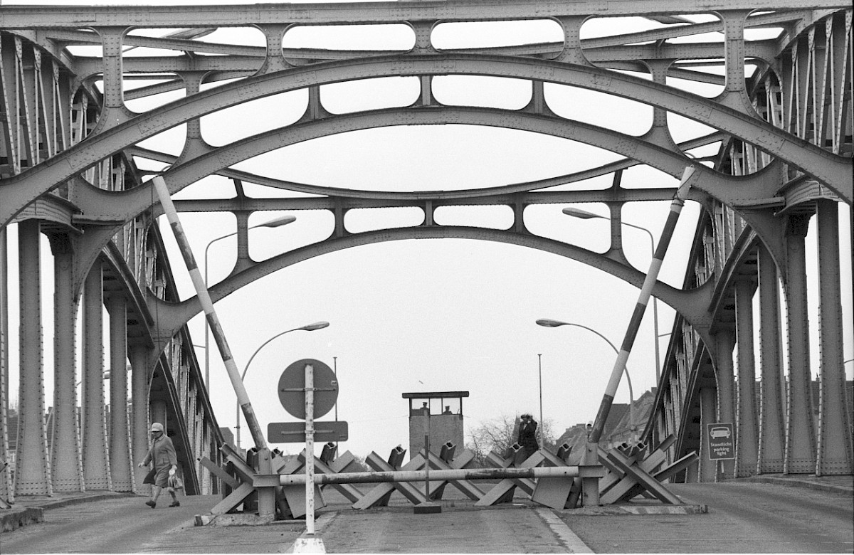 3 de mayo, 1979 | Ciudadanos cruzando el paso fronterizo de Bornholmer Straße por el puente Bösebrücke en Berlín. La carretera está dividida con dos barreras. Dos soldados fronterizos en una atalaya vigilan el paso fronterizo. #UnMundoDividido