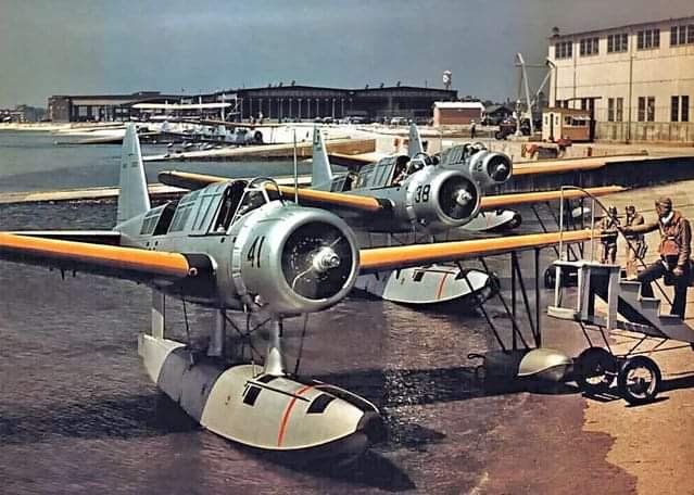 A flight of three US Navy Vought OS2U Kingfisher seaplane spotter aircraft pull into the shore for a 'running crew change'. I particularly like the 'Air stairs' that are wheeled out into the shallows! I'm not quite sure how they cast off? 😂
