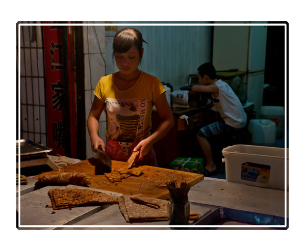 A #Chinese #street #seller preparing #bread to go with the #meat and #fish being prepared in #neighbouring #stalls, her #family member #relaxes behind the stall watching #tv #streetfood #streetfoods #streetfoodlover #China #PictureOfTheDay for more see darrensmith.org.uk