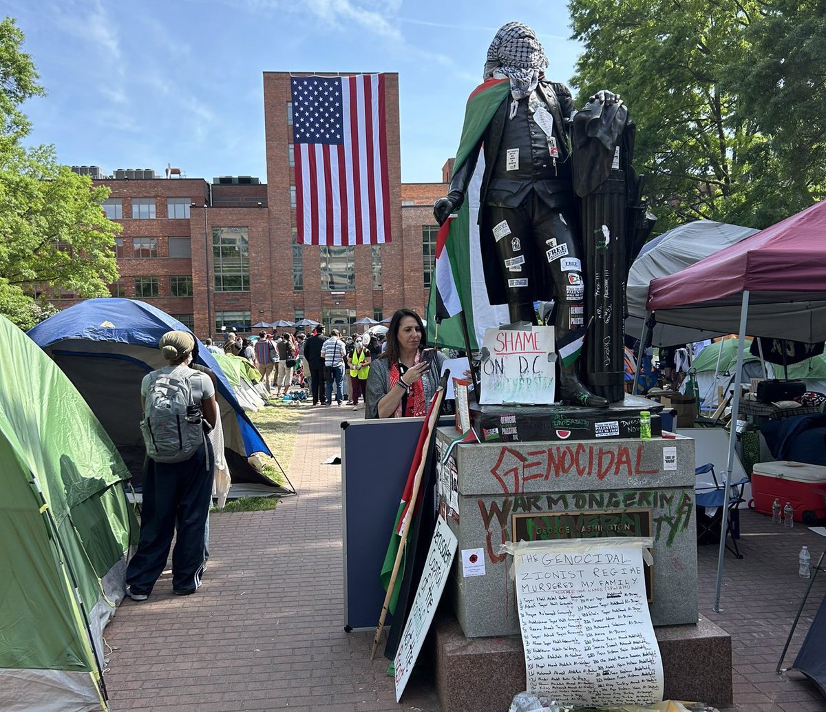 A Tale of Two Americas: George Washington statue stands desecrated, covered in a Palestinian flag, keffiyeh and graffitied with the words ‘Genocidal’ and ‘Warmongering.’ In the background, an American flag hangs off the GWU campus building.