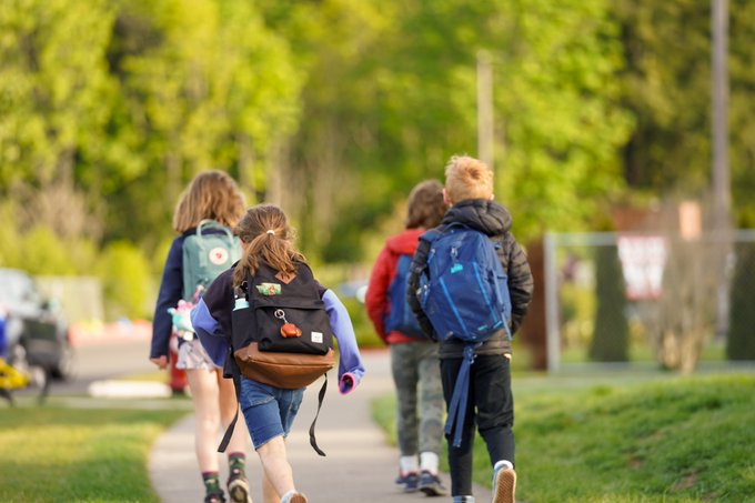 Four students with backpacks running toward school on sidewalk