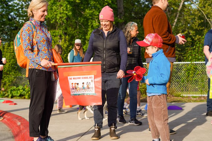 A crossing guard flag with a graphic on it is shared on sidewalk with onlookers