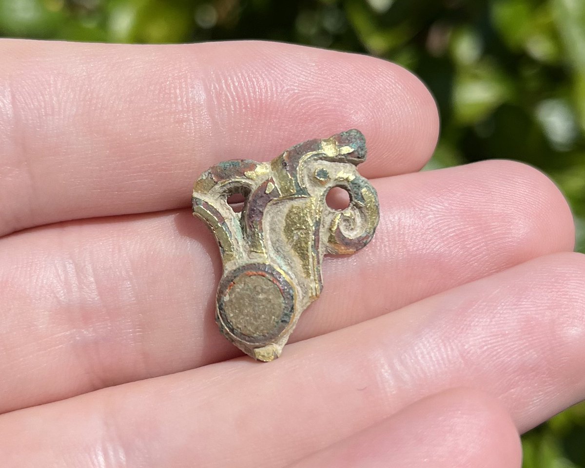 An incomplete Anglo Saxon gilt sleeve gusset plate with a raven head, originally two. The inlaid stone could be a dark amber.