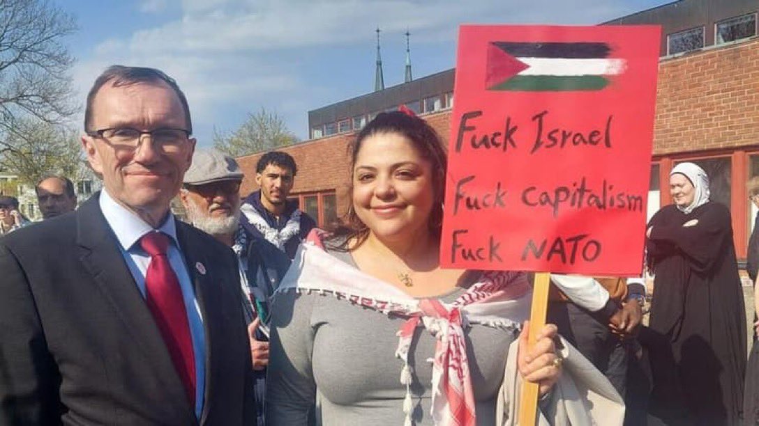 ▪️Fuck Israel, ▪️Fuck Capitalism, ▪️Fuck NATO says the sign 💥This is @EspenBarthEide, the Foreign Minister of Norway 🇳🇴, a @NATO member, standing smiling next to Mona Osman, the daughter of Abou Zayed,who is facing charges for murdering six Jews and wounding 22 in a Paris…