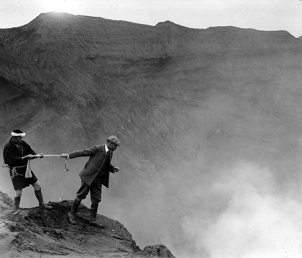 A man leaning over the edge to look over in to the crater of Aso San mountain, Kyushu, Japan, ca. 1906 by Herbert Ponting