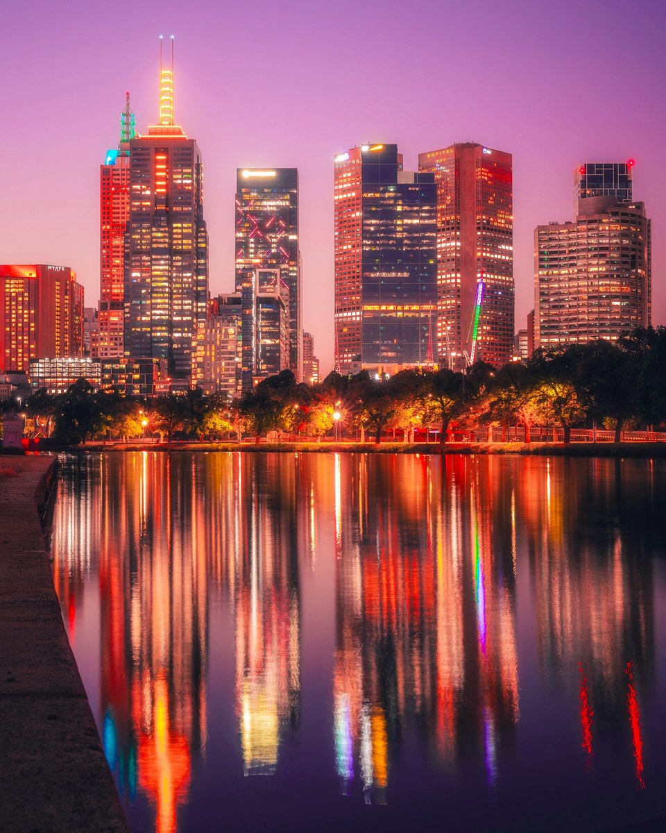 Melbourne's skyline looking electric ⚡️ 📍 Melbourne CBD, on Wurundjeri Country⁣ 📷 via IG/bryanrphotography [Image Descriptions: The image shows a city skyline at night with buildings illuminated. The skyline is reflected on a river, with the sun setting in the background.]