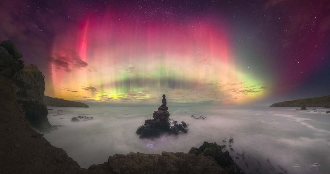 This well-composed composite panoramic view looks due south from Banks Peninsula near Christchurch on New Zealand's South Island. The base of a tower-like rocky sea stack is awash in the foreground, with stars of the Southern Cross at the top of the frame and planet Earth's south