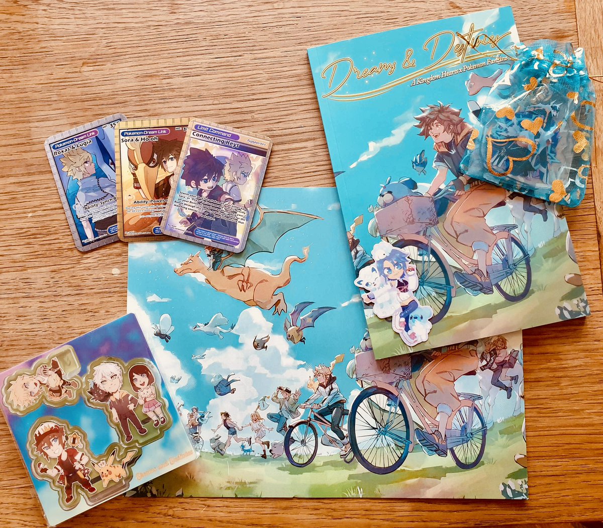 My copy of the <a href="/KHxPokemonzine/">Dreams and Destinies: A KH x Pokemon Zine</a> finally came, it’s always so cool seeing my art physically, everyone’s art turned out so good and the merch goodies are chefs kiss 🫶