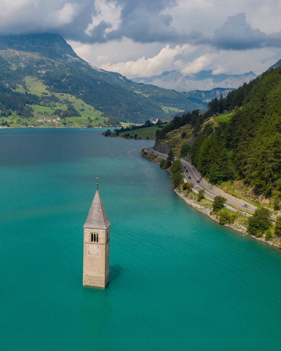 23. The Curon bell tower rises from Lake Resia, Italy. 

In 1950, against protests and even the Pope's plea, authorities flooded the valley for a hydroelectric plant. 

Homes, farms, and history vanished, but the tower endures, a lone witness to the submerged village of Curon.