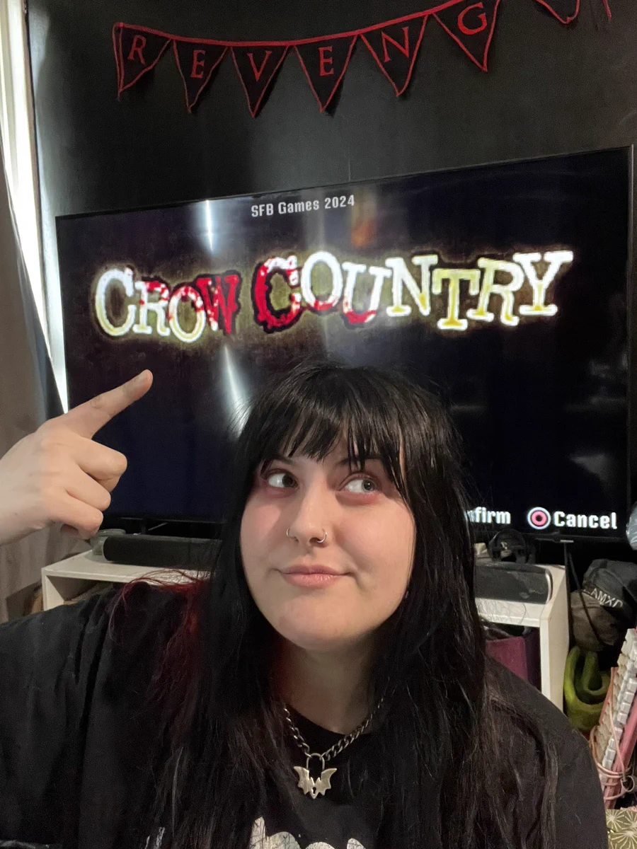 Georgie smiling and pointing to the TV behind her showing the start menu for Crow Country