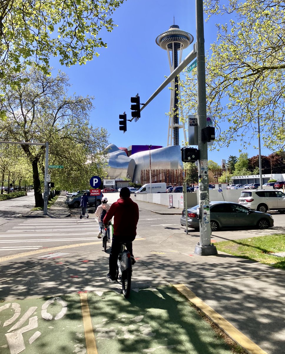 Here's what this gap looks like. It's a two way protected bike lane that dead ends in a parking lot. Forcing people trying to get to the Seattle Center, like this family out for a 🚴🏻‍♀️🛴, to choose between a dangerously fast street, a narrow sidewalk, or a parking lot.