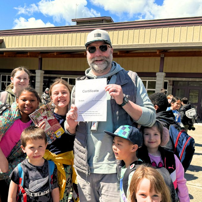 Josh Triplett holds certificate outside school and is surrounded by smiling students