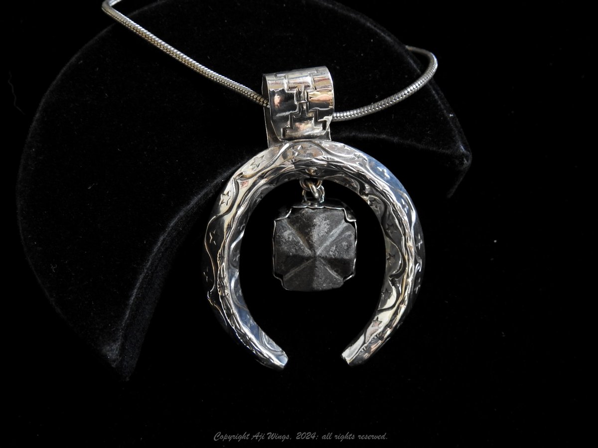 It's a classic naja-style pendant formed of heavy-gauge sterling silver triangle wire, formed and stamped freehand on both upper angles, plus the very apex; hand-made bail; and a pendant suspended from the center, holding a bezel-set staurolite, a rare mineral: