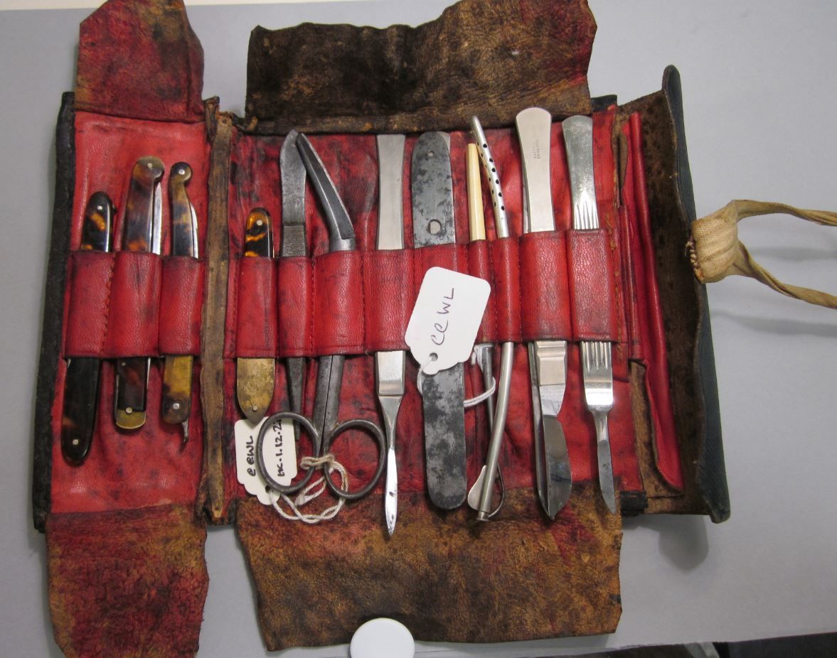 This is a travelling leather operating case from the 19th Century. wrapped in a surgical canvas kit. The kit includes instruments such as five scalpels and four folding fleams/razors. The instruments are from a range of different instrument makers.