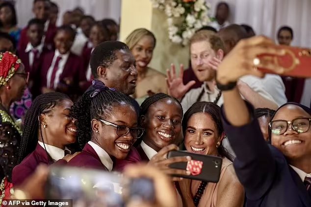 Meghan poses for selfies with students, while Harry photobombs her in the background.