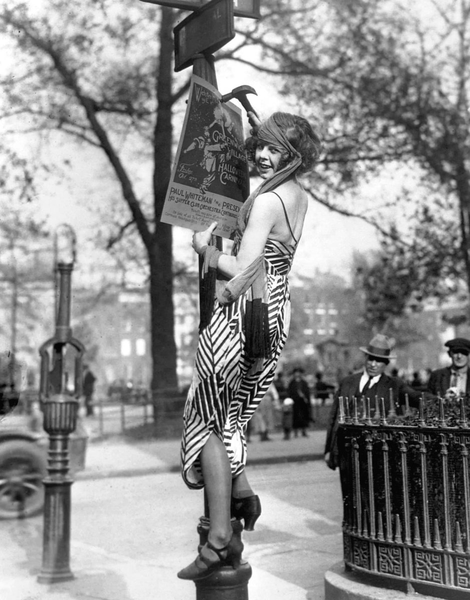 c.1922 A gussied up flapper hangs a poster advertising the Greenwich Village Halloween Ball. The neighborhood keeps the spooky spirit alive to this day, hosting the Village Halloween Parade, a street parade and pageant that has occurred every year since 1973.
