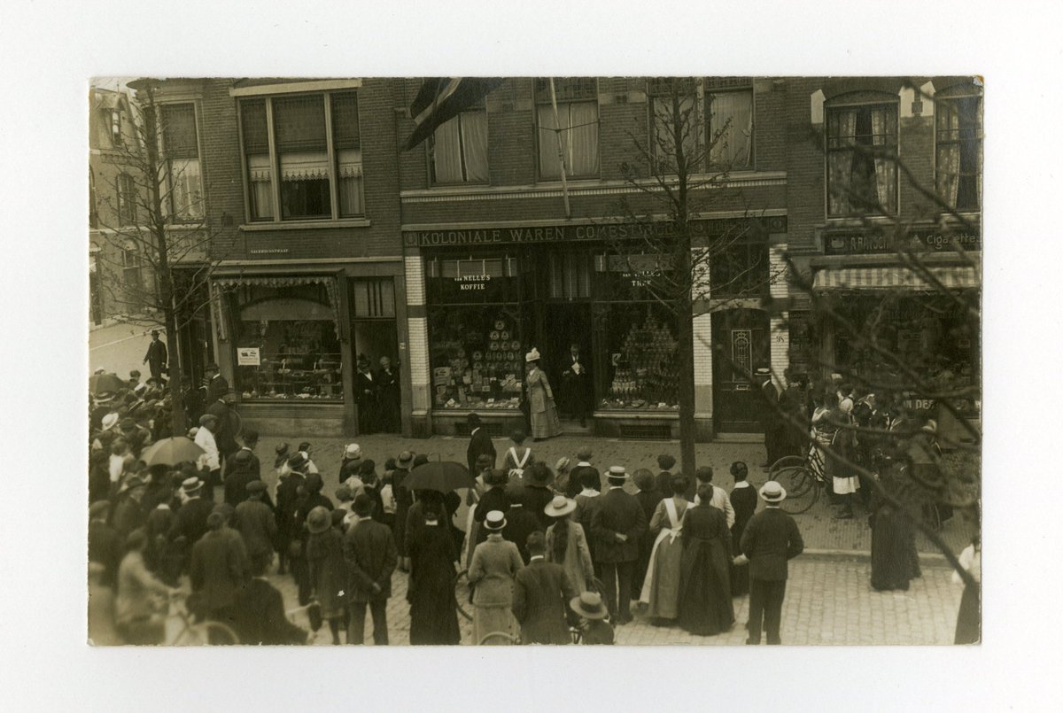 Ook koningin Wilhelmina ging soms uit winkelen. Op 11 mei 1916 was het Winkelweek in de Valeriusstraat in Den Haag. Buurtbewoners dromden samen voor de kruidenierszaak van Louis Retel om een glimp van het koninklijk winkelbezoek op te vangen. Foto @haagsarchief