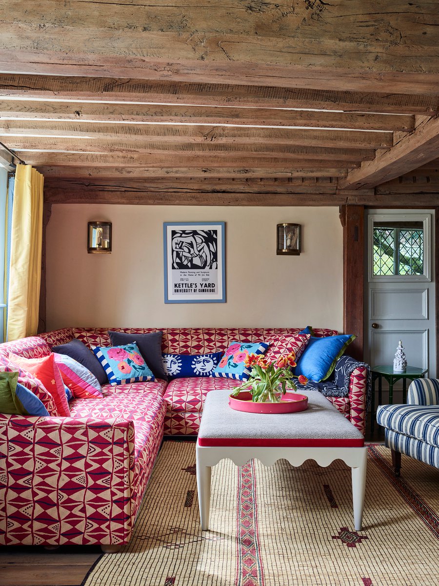 A charming 15th-century home in Sussex gets a colourful overhaul by Phoebe Hollond. In the playroom, the red trim from Samuel & Sons on the footstool tones with the sofa in Le Manach's ‘Benin’: trib.al/zrTVP7A