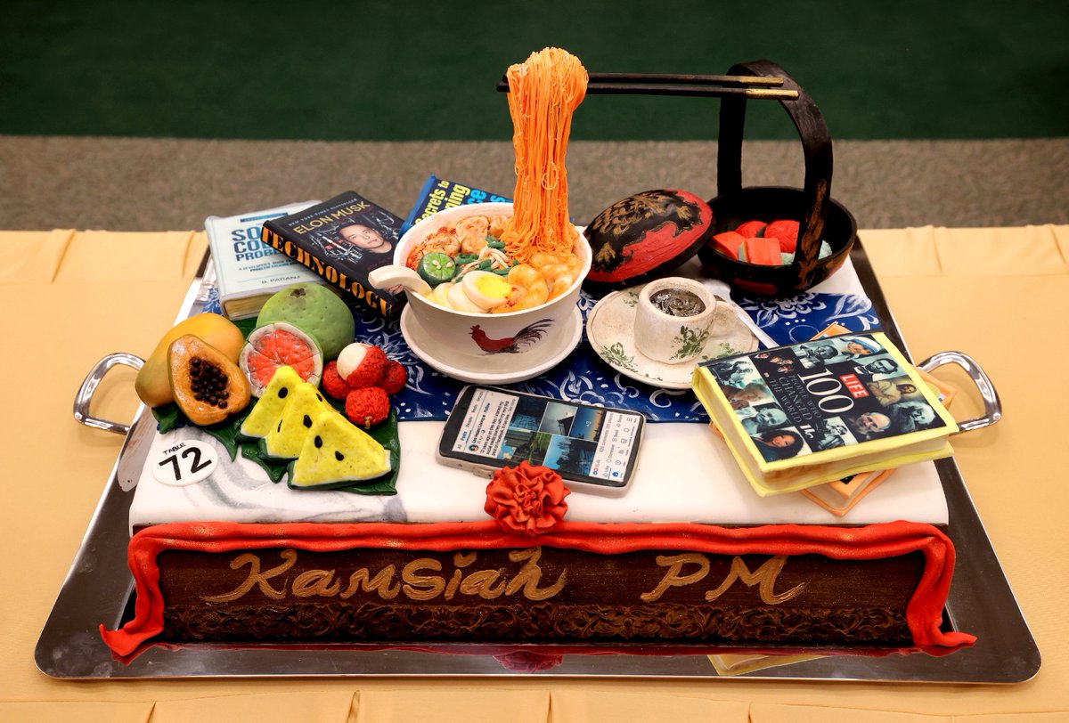 Outgoing Singapore Prime Minister Lee Hsien Loong's retirement cake features a bowl of seafood rice noodles, a cup of tea, tropical fruits, Elon Musk biography by @ashleevance, the book '100 people that changed the world' and a phone featuring his twitter account @leehsienloong