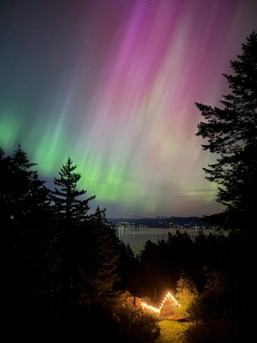 Northern lights seen from high vantage point over looking water, a cabin, and Bellingham city line