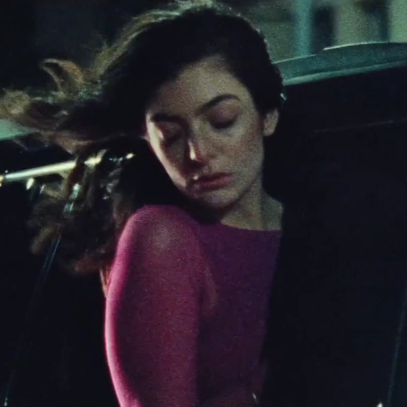 A cinematic shot of a woman with long dark hair wearing a pink sweater, appearing dazed or unconscious as her hair blows in the wind at night.