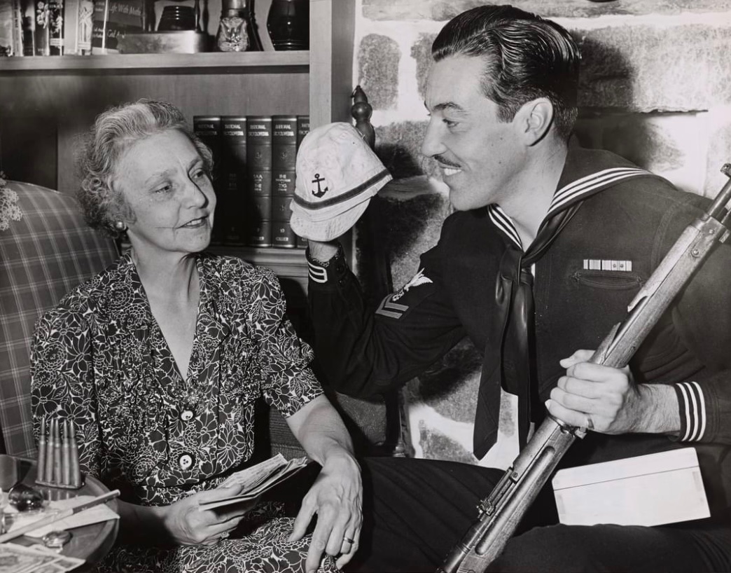 Coast Guardsman Cesar Romero, aka “The Joker”, proudly exhibits his wartime souvenirs to his mother. 🇺🇸 The Japanese cap and gun came from the Saipan and Tinian invasions in the Marianas.⚓️