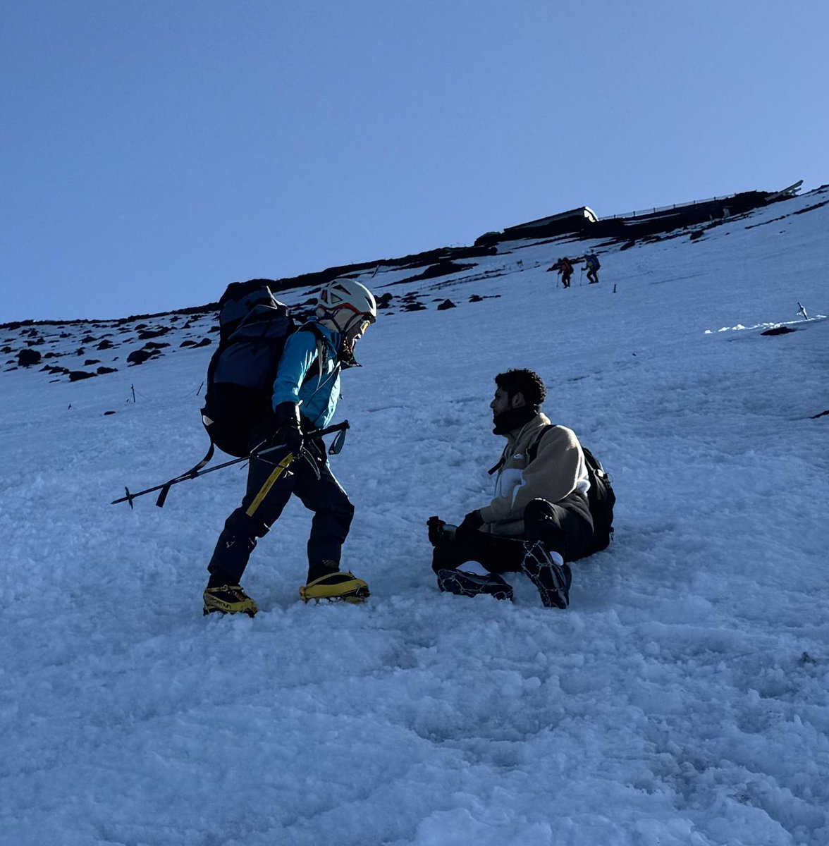 red_mattsun's tweet photo. 富士山にて、山頂から下降中に座り込んでモゾモゾする人影を見つけました。午後になり気温が下がりクラストし始めた雪面にチェーンスパイクをはいた外国人の登山者。大丈夫？と聞くと怖くて立てない、降りられないと言う。アックスも��く固くなり始めた雪面で滑ったら止まれず助からないかもしれない https://t.co/5PwMq43wI9