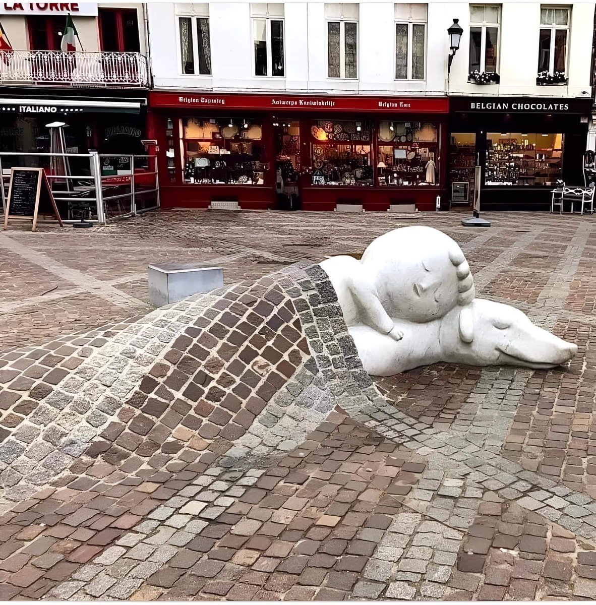 White marble sculpture of Sleeping Nello and Patrasche (Dog of Flanders), covered by a blanket of cobblestones, in front of the Cathedral of Our Lady, Antwerp, Belgium 🇧🇪 Beautiful 😍 ❤️