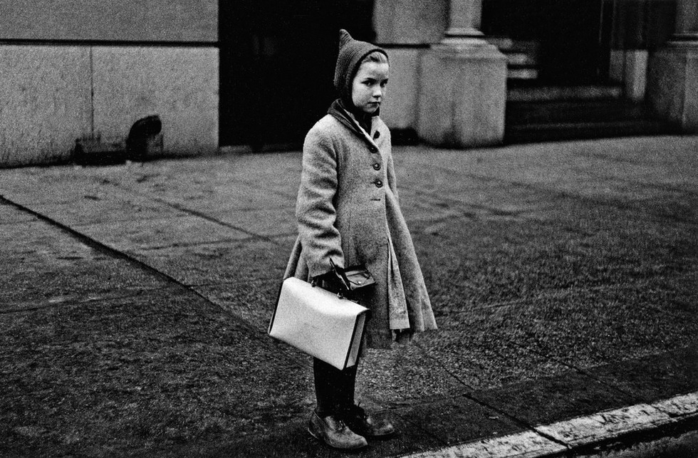 Diane Arbus, Girl with a pointy hood and white schoolbag at the curb, N.Y.C. 1957