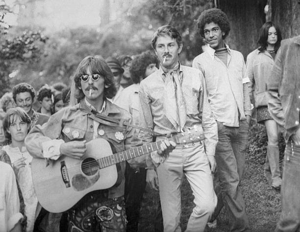 George Harrison strums a borrowed guitar as he is followed by local hippies strolling through Golden Gate Park. Harrison, visiting San Francisco, spent an hour touring the hippie Haight-Ashbury district culminating this stroll through the park.