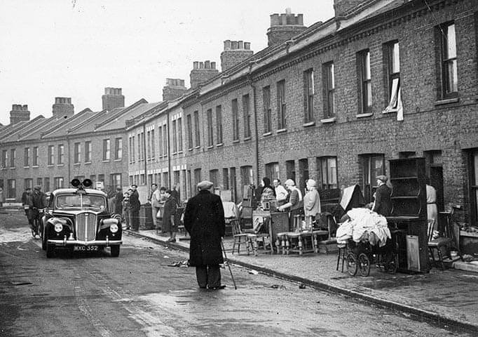 A photograph from circa 1953 as a police car drives through Mary Street in Canning Town, London, warning the public that 20 tins of highly dangerous hydrocyanide had been washed from the dockside in the aftermath of floods